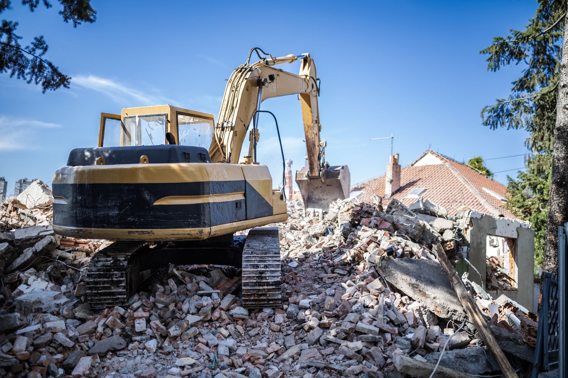 Yellow excavator demolishing a building on a sunny day.