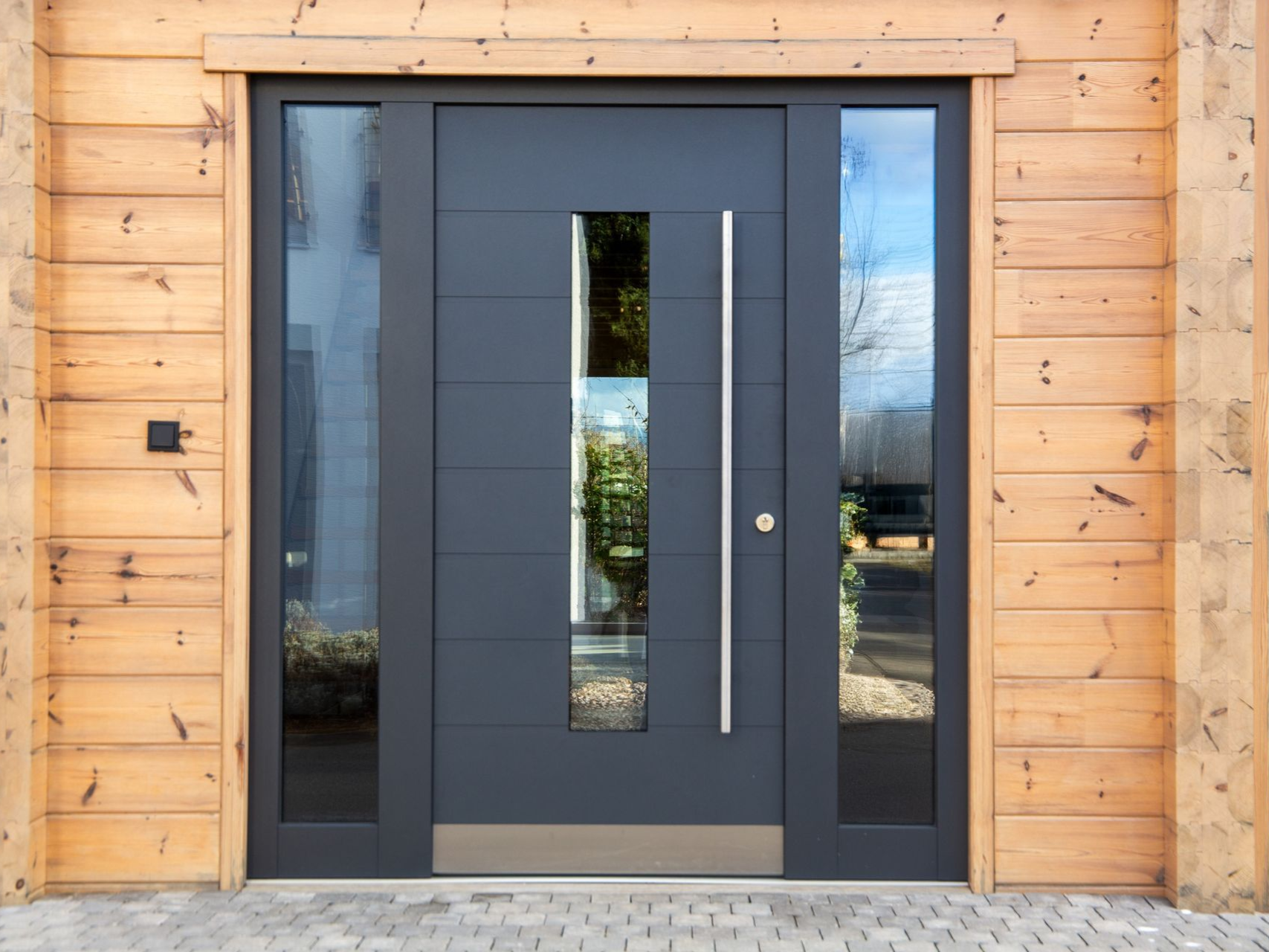Gray front door with sidelights, set in a light wood frame.
