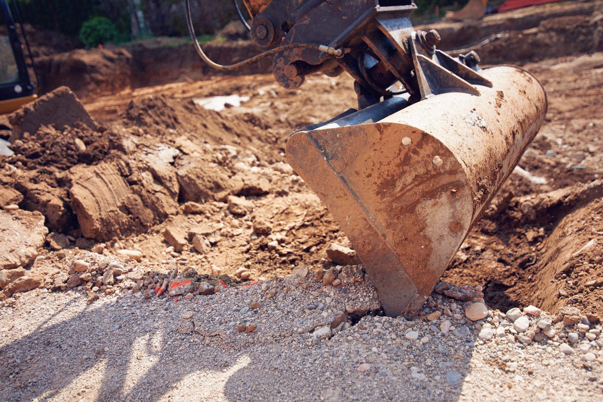 A backhoe bucket scoops dirt from a construction site, near a trench.