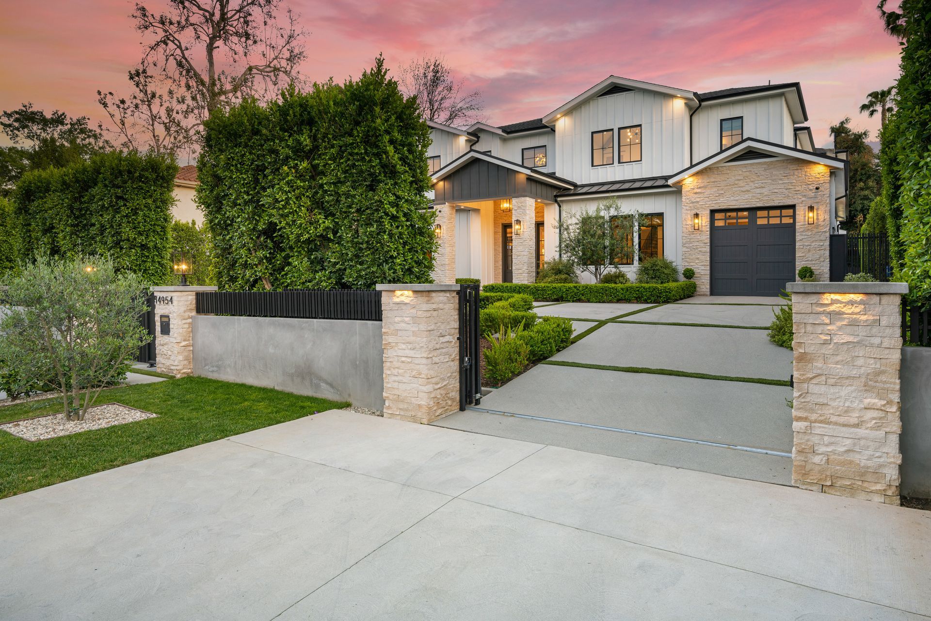 Luxurious two-story white house with a stone facade, gray garage door, and a concrete driveway at sunset.