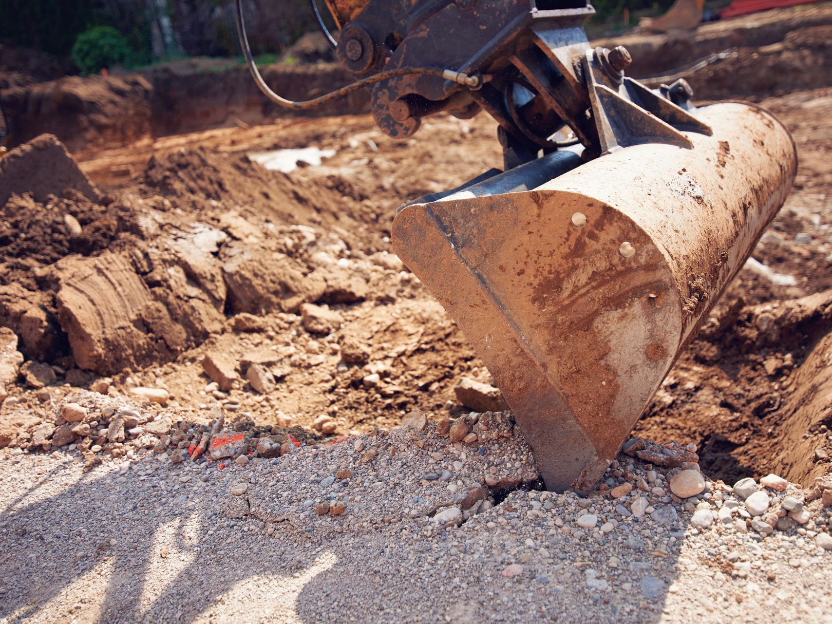 Excavator bucket in close-up, scoops earth and gravel at a construction site.