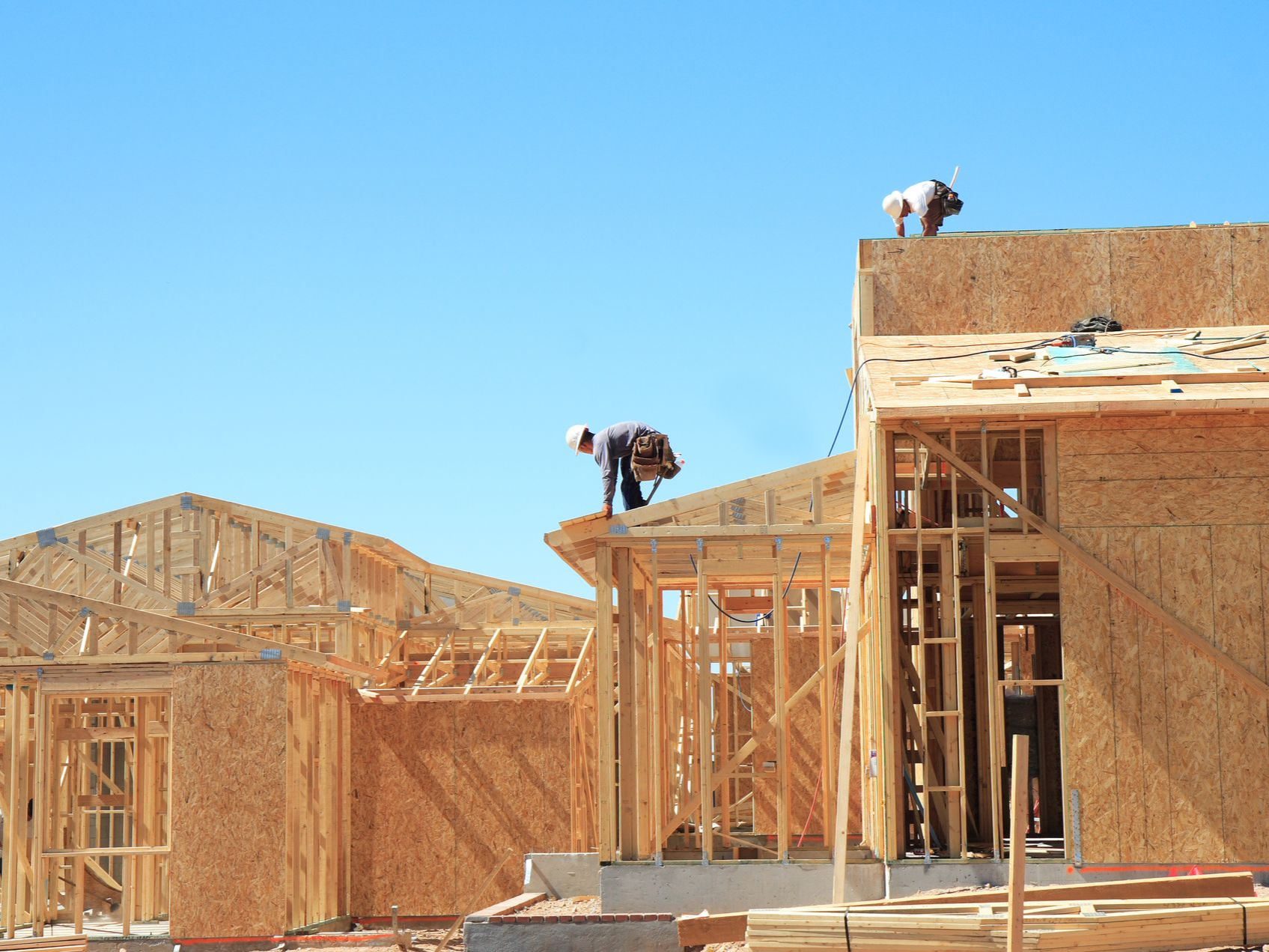 Construction workers on a house frame, under a clear blue sky.