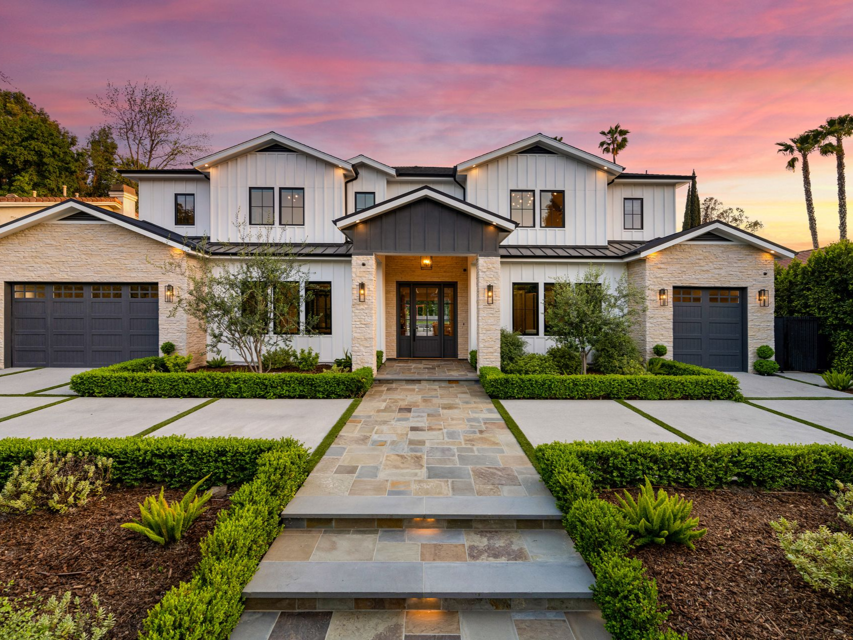 Luxurious white house with gray accents and stone pathway at sunset.