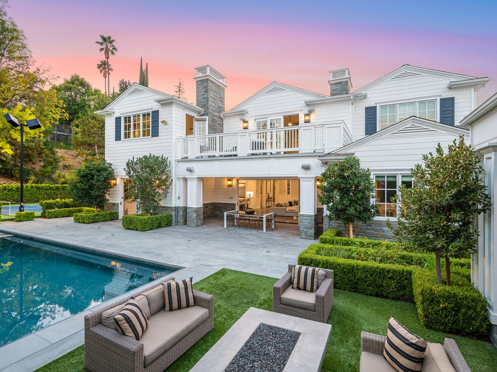 Luxury home exterior with pool, patio furniture, and manicured lawn at sunset.