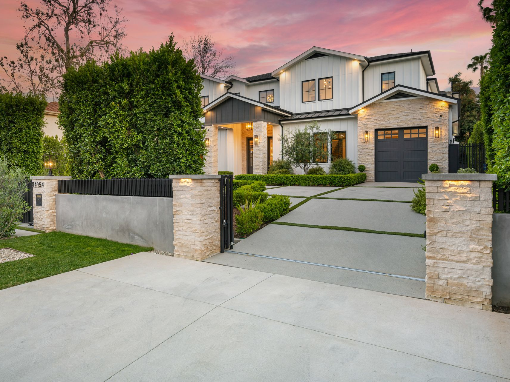 Modern white house with dark trim and stone accents at sunset, concrete driveway.