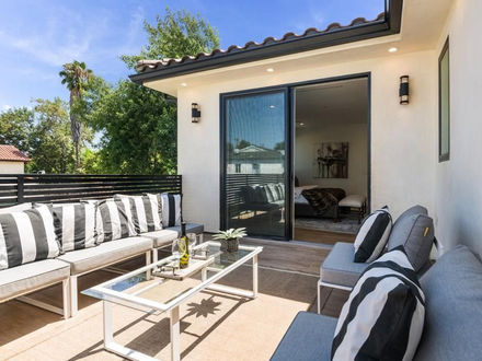 Patio with outdoor seating, black and white striped pillows, and glass table; sliding door to interior.