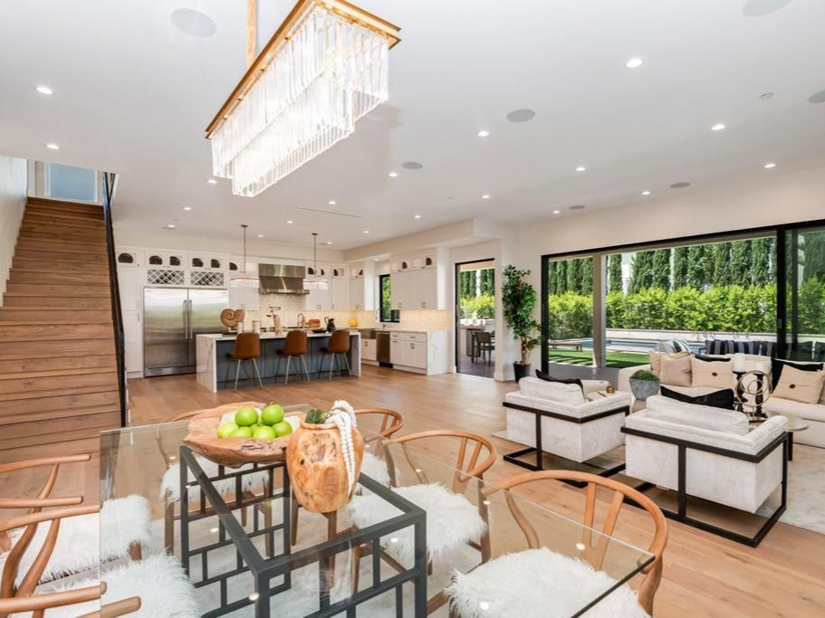 Spacious modern home interior with open kitchen, dining, and living areas; large windows, wood floors, and a modern chandelier.
