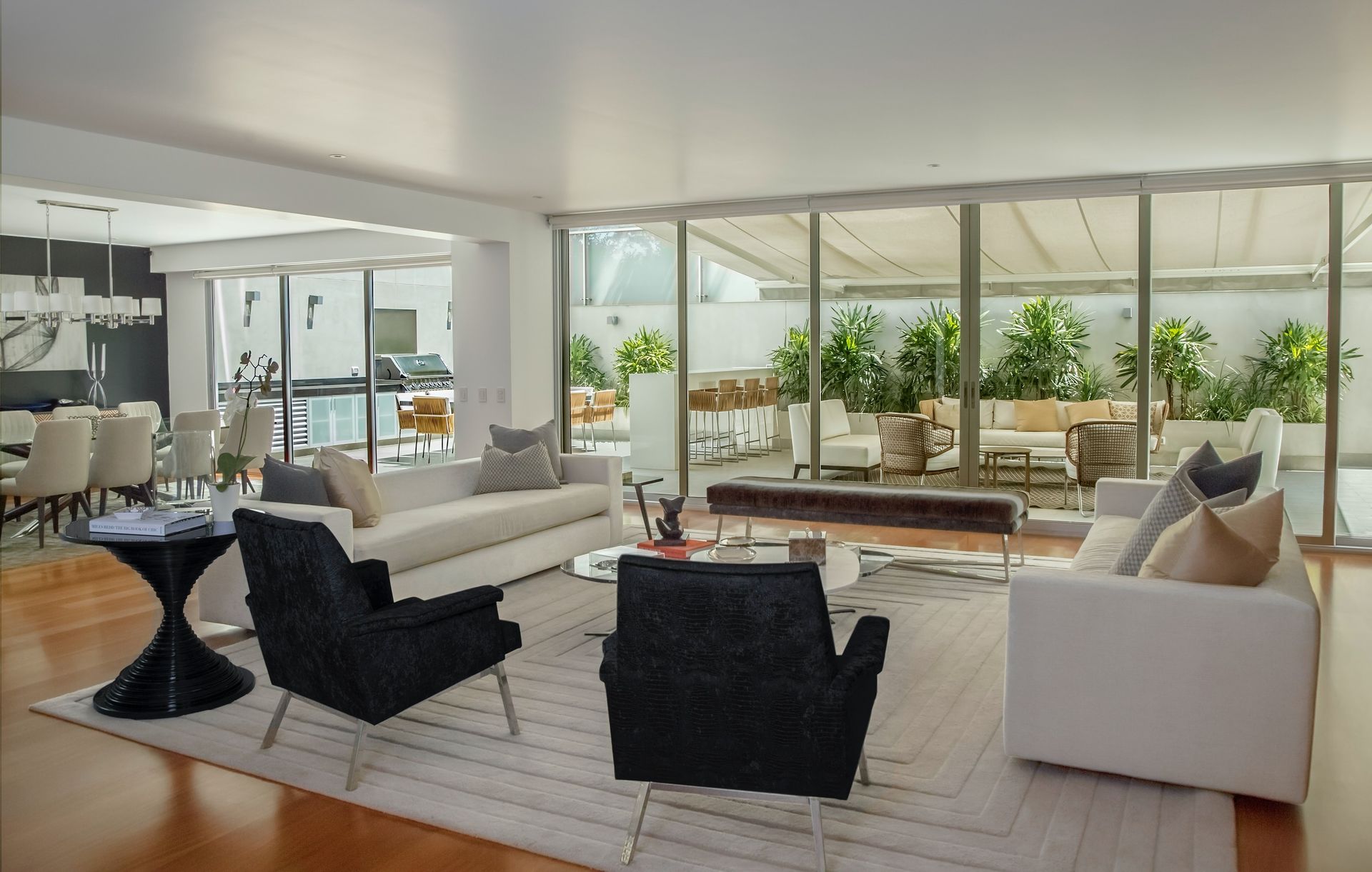 Elegant living room with white sofas, black armchairs, and a view of an outdoor patio.