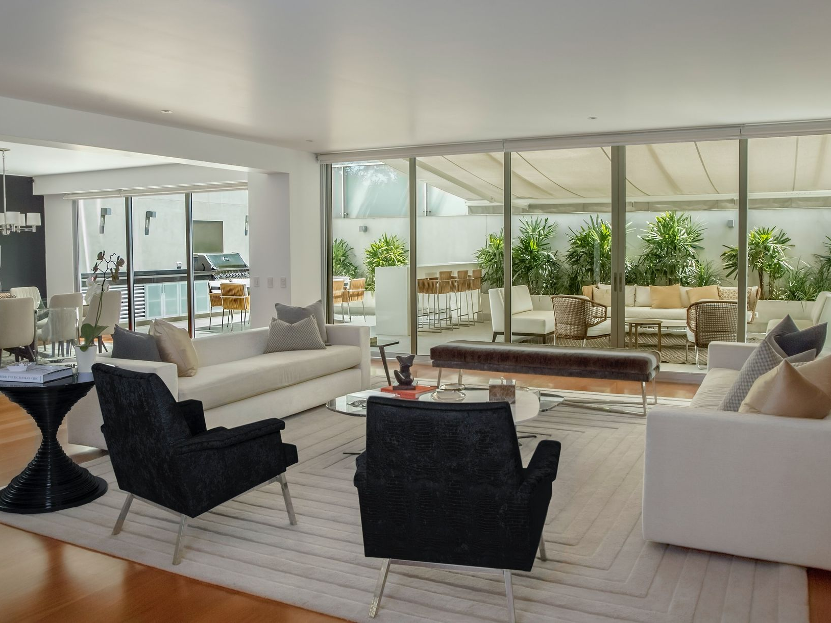 Bright living room with white sofas, black chairs, and a patio view.