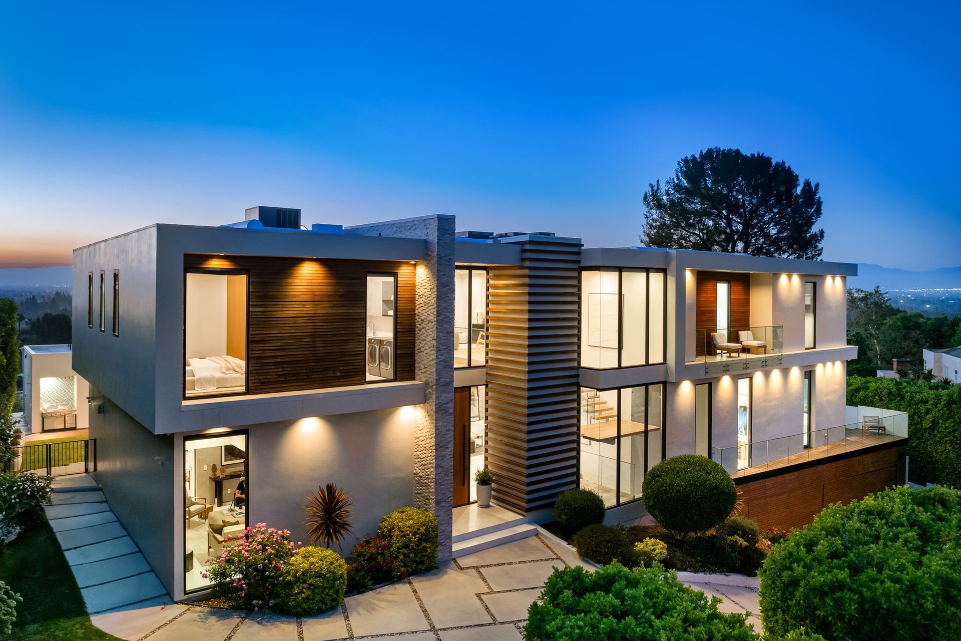 Modern two-story house with illuminated exterior, wooden accents, and large windows at dusk.