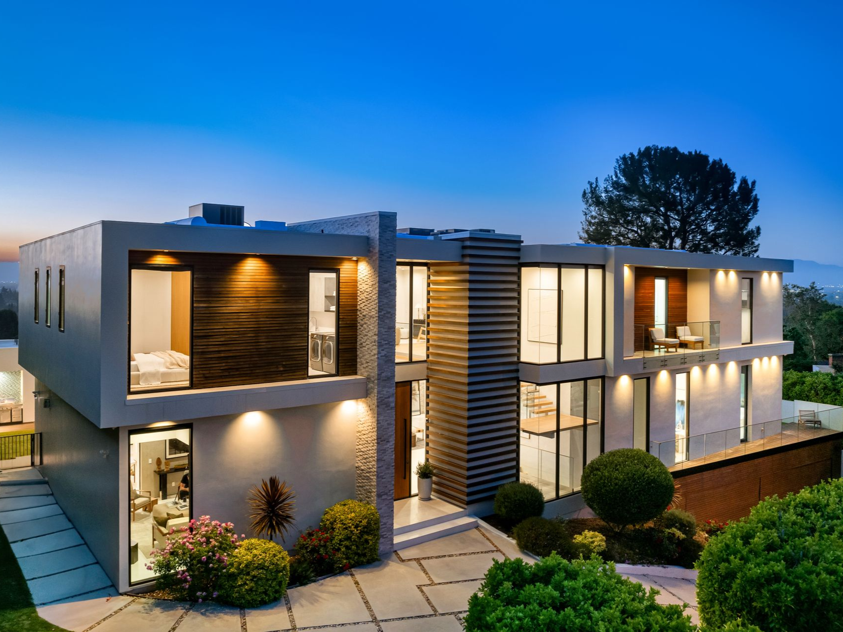 Modern two-story house with illuminated windows and a stone walkway at dusk.