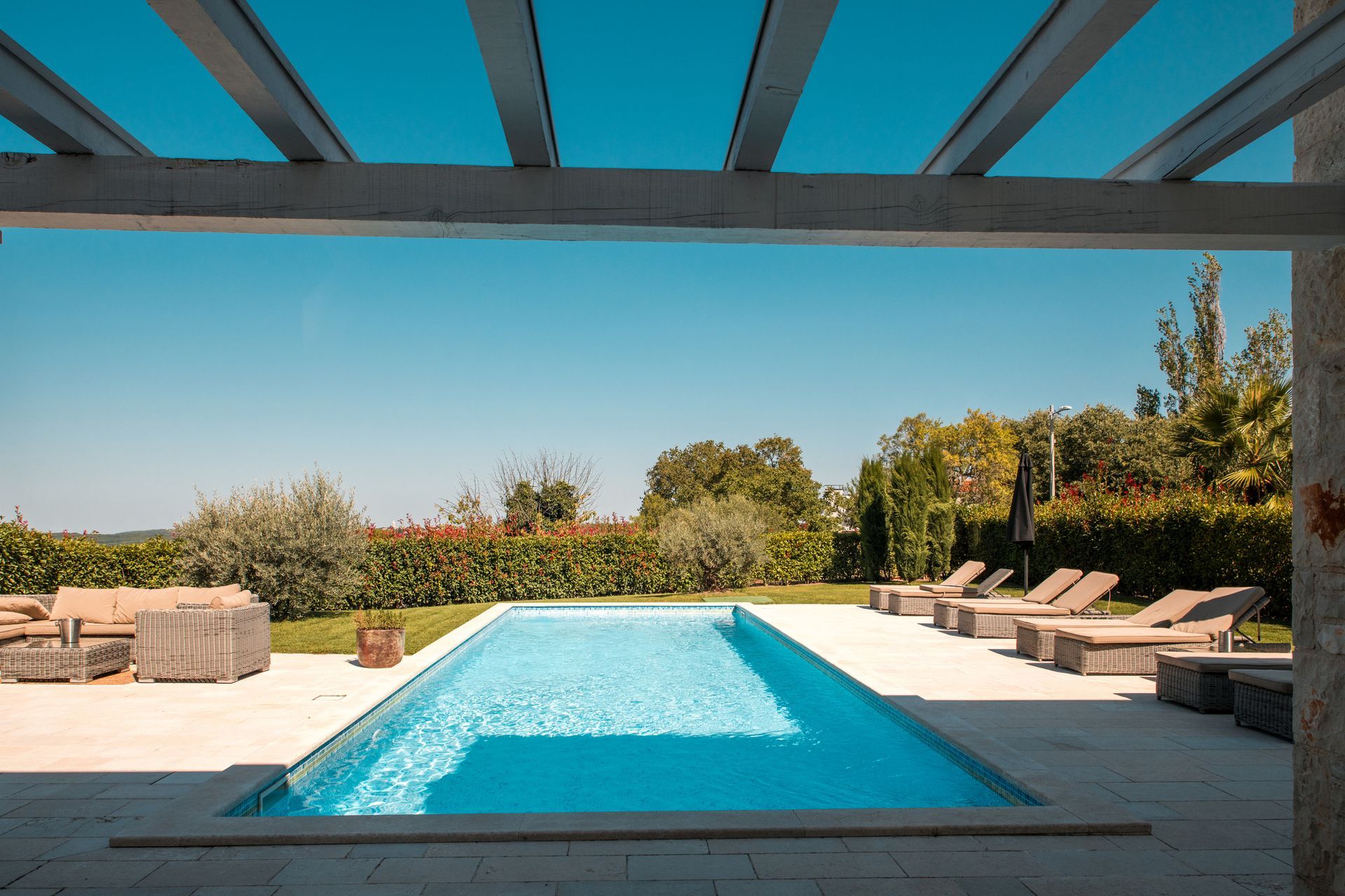 Pool and patio with lounge chairs and pergola, under a bright blue sky.