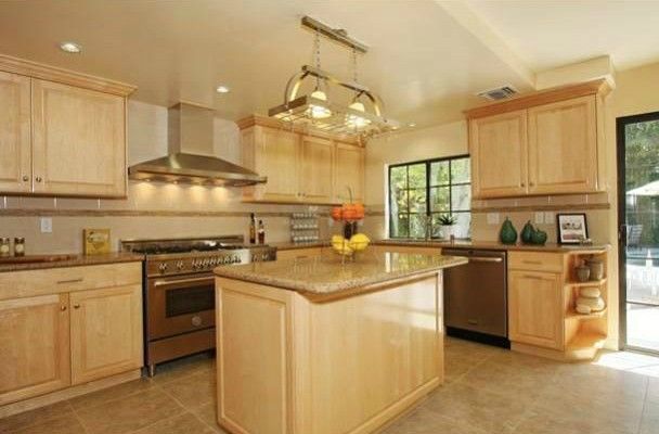 Kitchen with light wood cabinets, stainless steel appliances, and island with granite countertop.