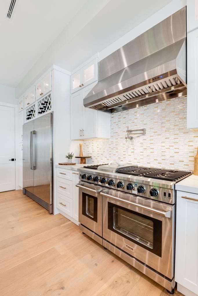 Modern kitchen with stainless steel appliances, white cabinets, and light wood floors.
