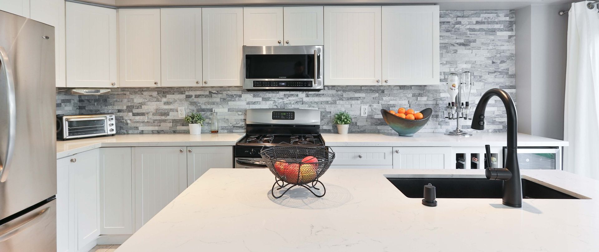 Modern kitchen with white cabinets, stainless steel appliances, and a gray brick backsplash.