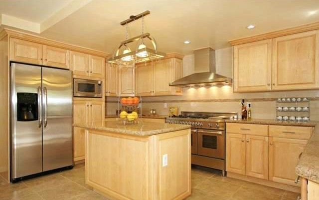 Kitchen with light wood cabinets, stainless steel appliances, and island with granite countertop.