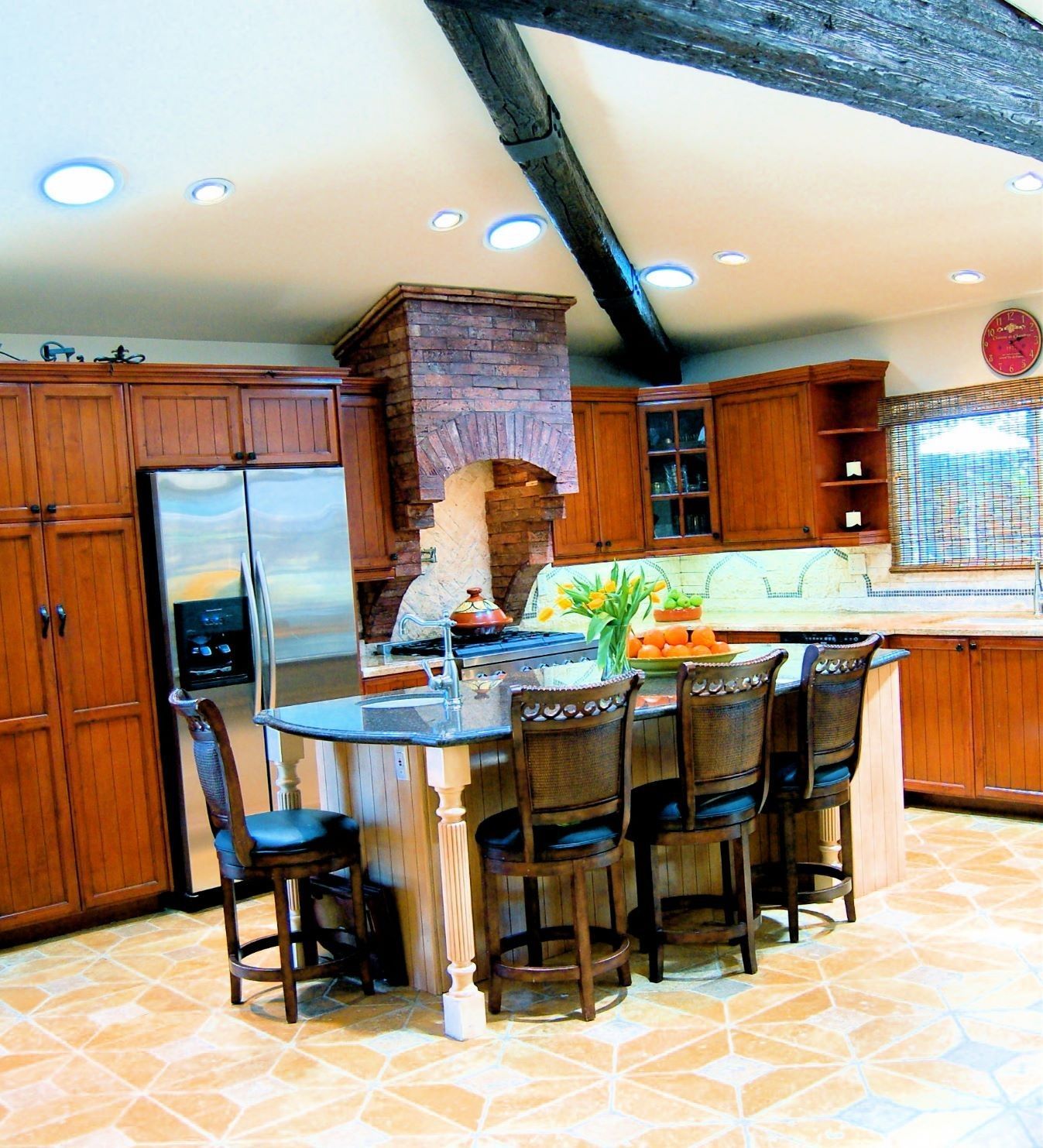 Kitchen with wood cabinets, island with stools, stainless steel fridge, and a brick range hood.