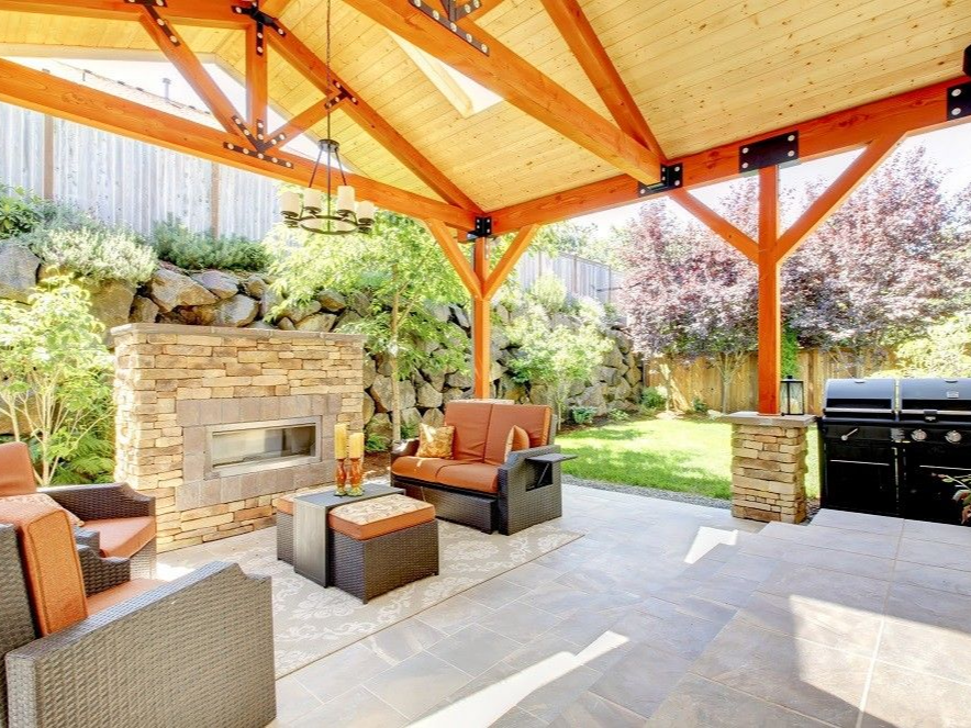 Patio with seating, fireplace, and grill under a wooden roof.