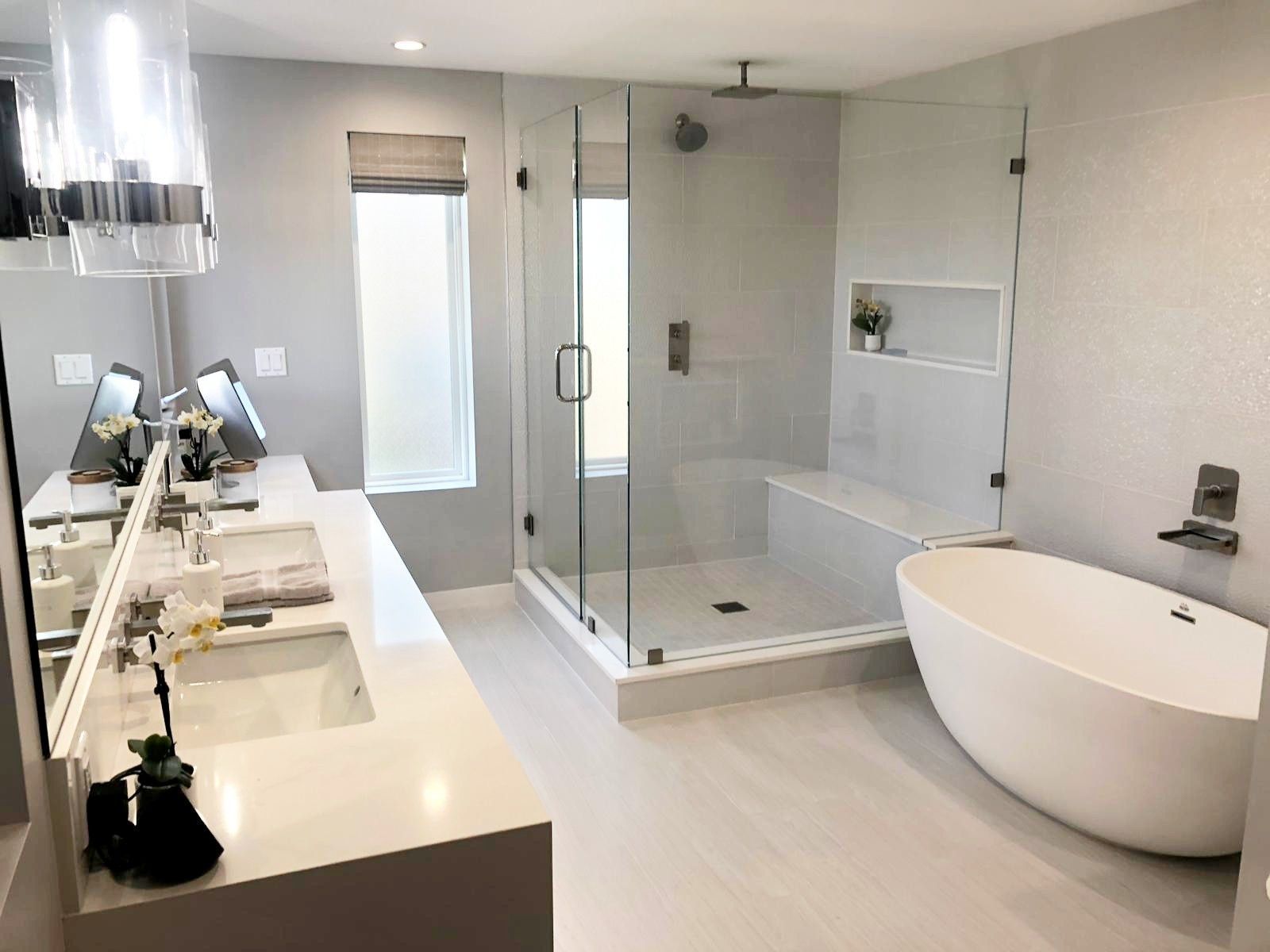 Modern, all-white bathroom with a walk-in shower, freestanding tub, double vanity, and a window with blinds.