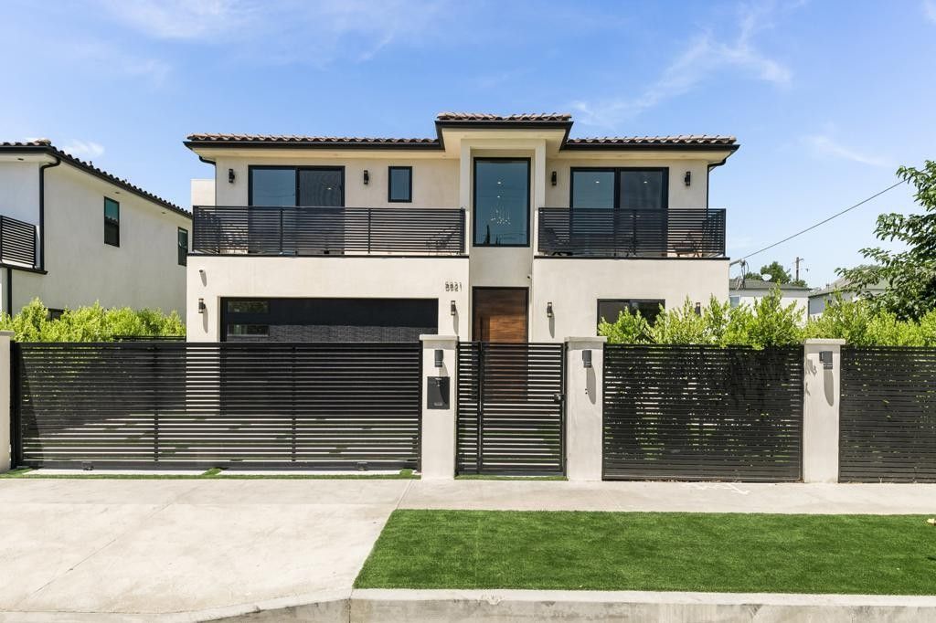 Two-story modern home with black fence, balcony, and garage on a bright, sunny day.
