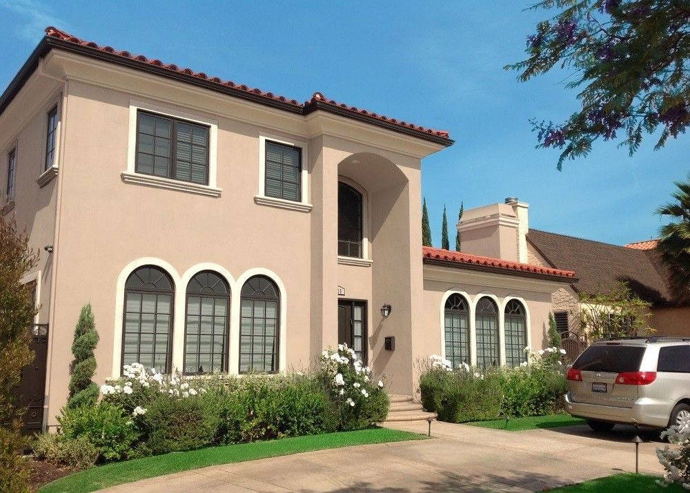 Beige stucco house with arched windows, red tile roof, and white car parked in driveway.