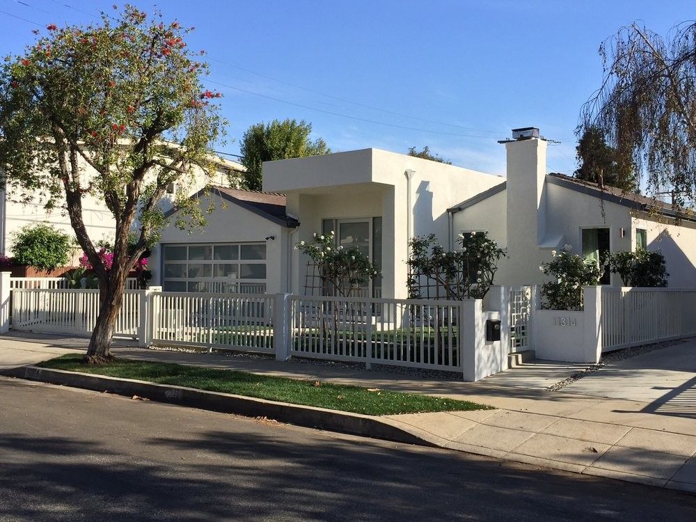 White house with a modern design, fence, and a tree on a sunny day.