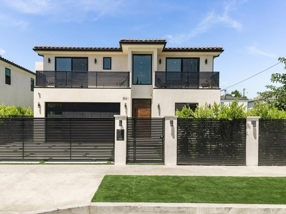 Modern two-story house with black trim, balconies, and a horizontal-slat fence. Bright, sunny day.