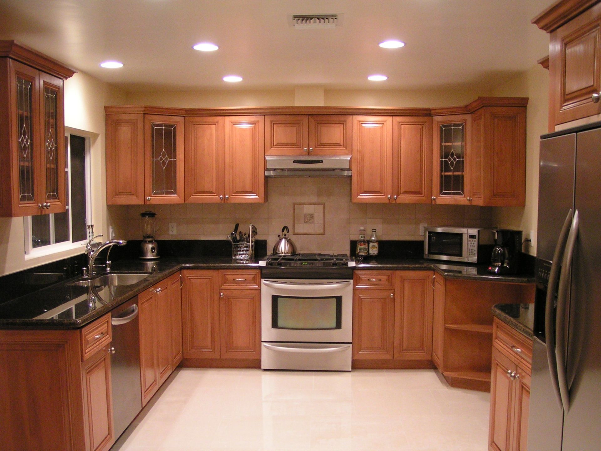U-shaped kitchen with light brown cabinets, stainless steel appliances, black countertops, and recessed lighting.