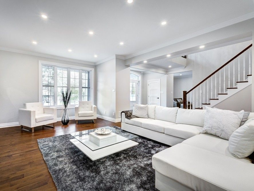 Living room with white sofa, rug, and coffee table; wooden stairs and floor.