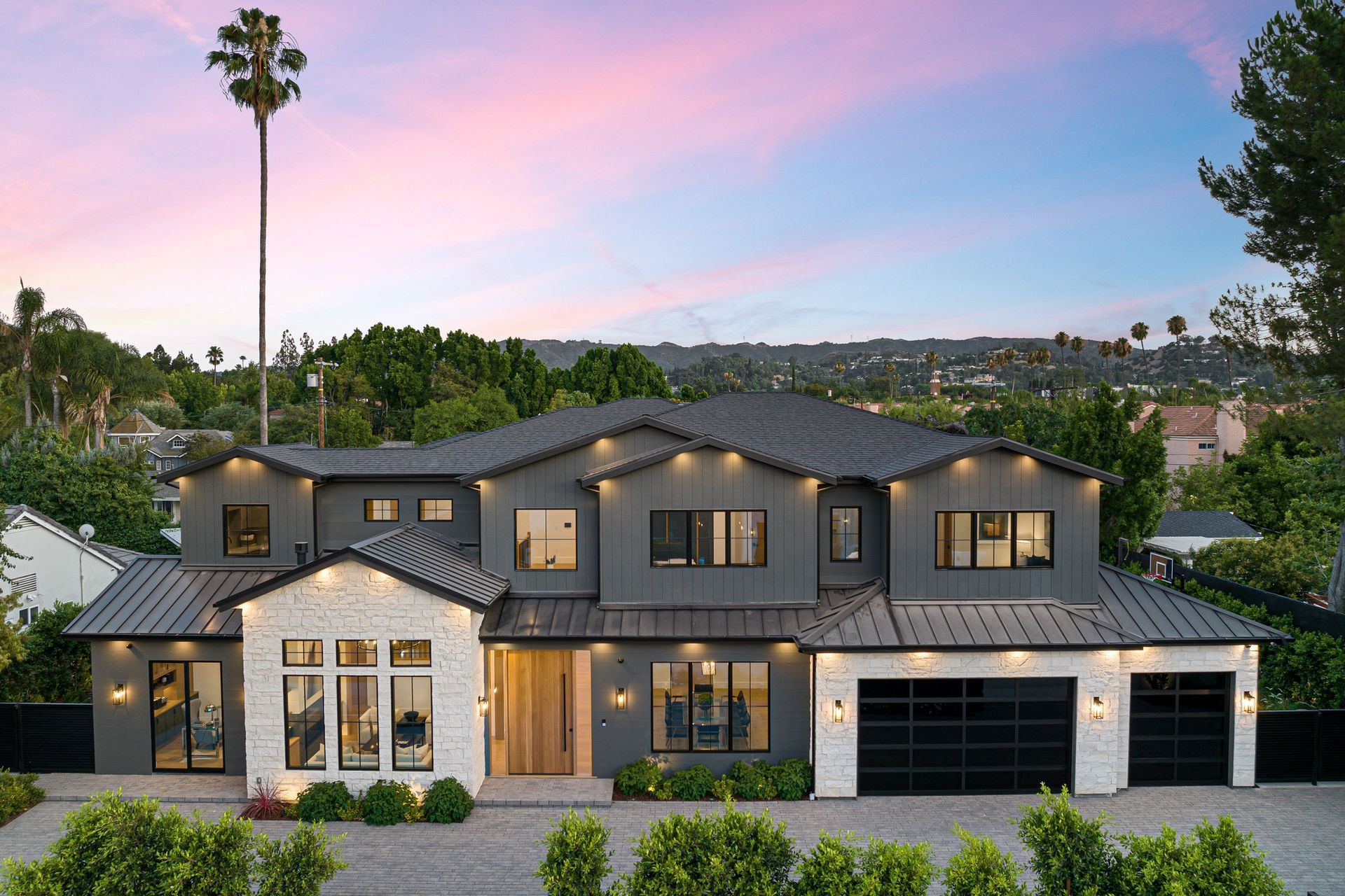 Two-story modern home with stone and wood accents, dark garage doors, and manicured landscaping in a blue hour setting.