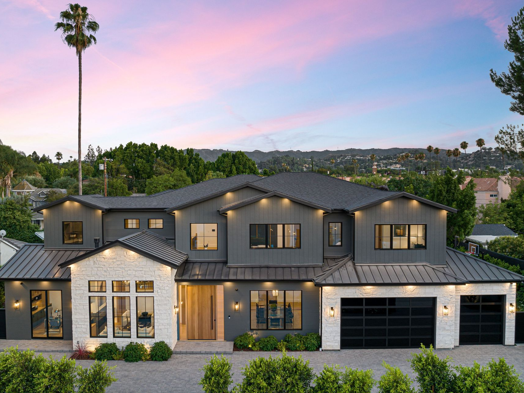 Modern gray and white house with black garage doors, under a colorful sunset sky.
