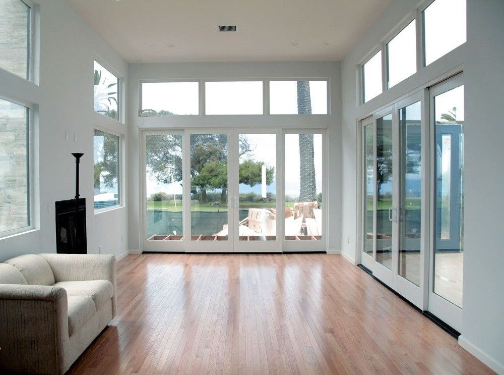Bright, modern living room with large windows, sliding glass doors overlooking a backyard, and a light-colored wood floor.