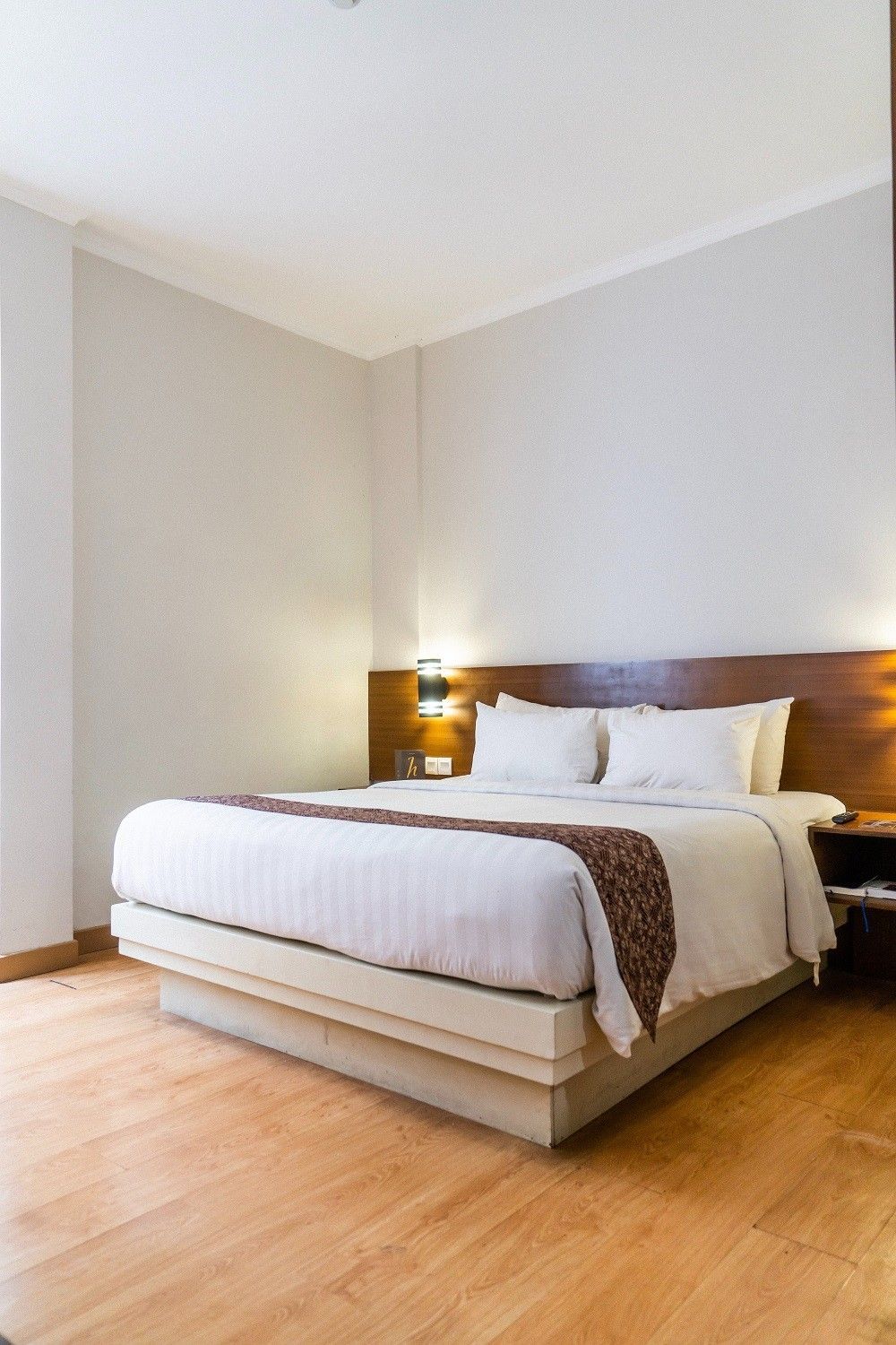 Hotel room with a bed, hardwood floor, white bedding, and wood headboard and nightstand.