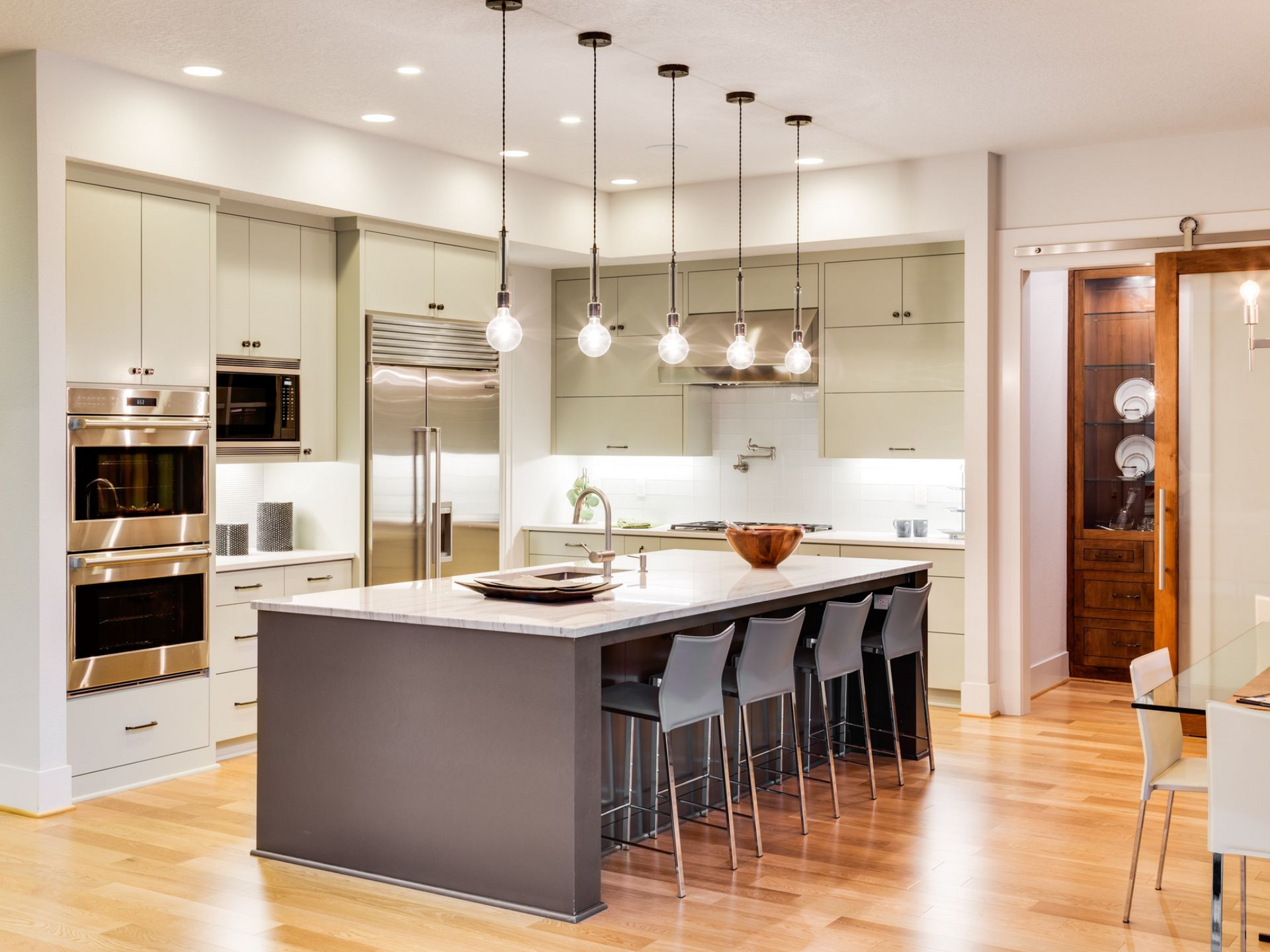Modern kitchen with island, pendant lights, stainless steel appliances, and wooden floors.