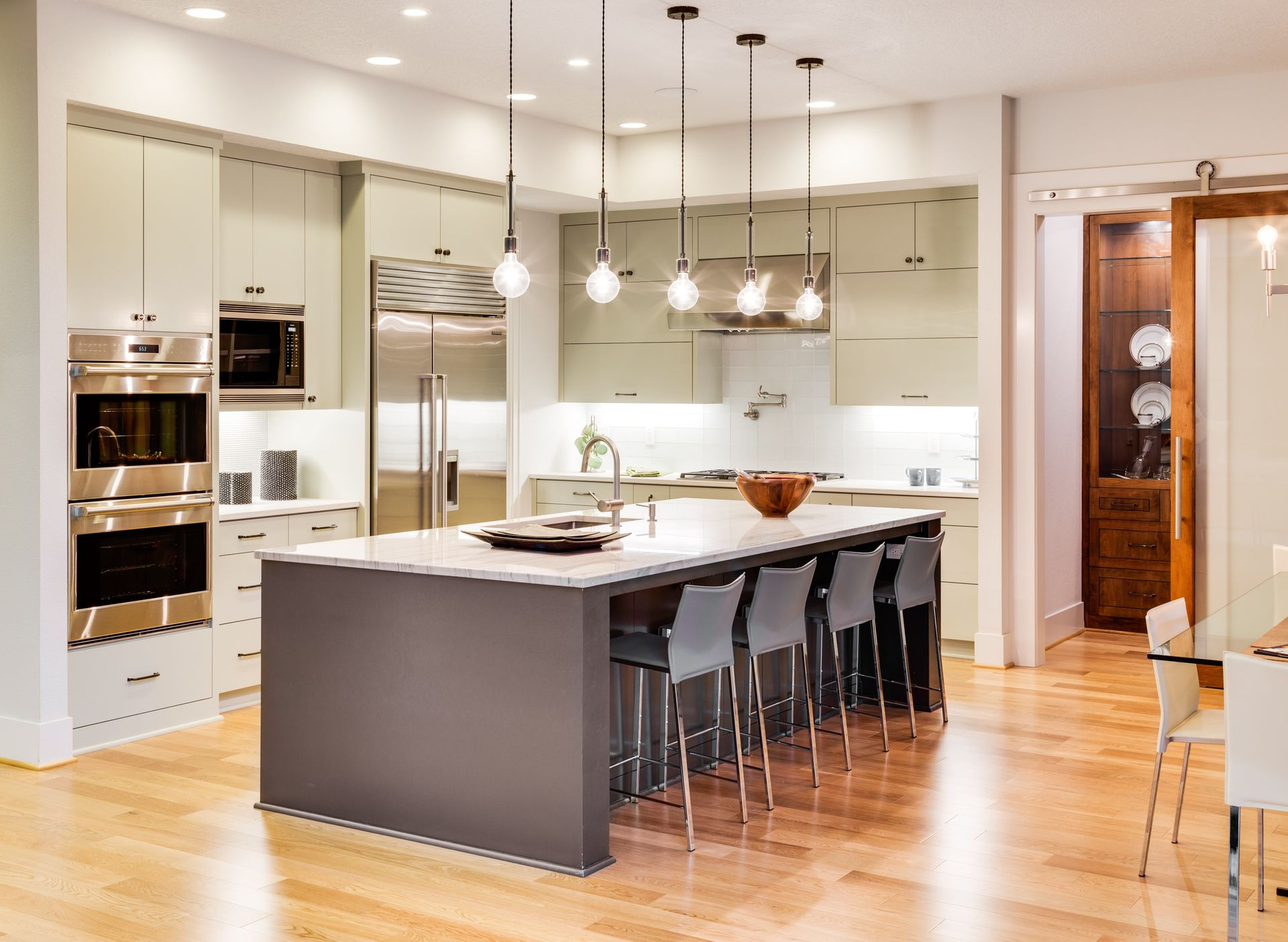 Modern kitchen with light green cabinets, stainless steel appliances, and a gray island with seating.