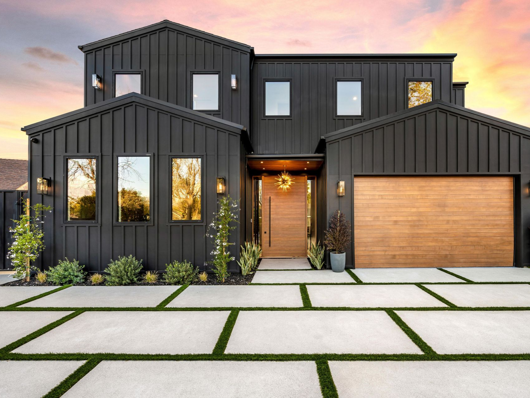 Modern black house with wooden door and garage, concrete pavers with green grass.
