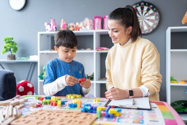Teacher helping child with colorful blocks at a table in a bright classroom