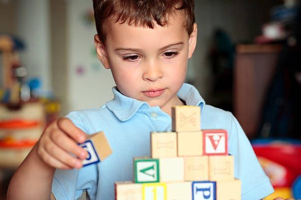 Child arranging colorful letter blocks on a table, focused on building a tower.