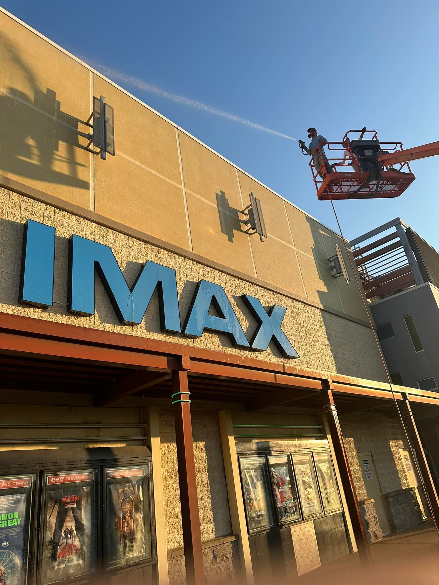 IMAX theater entrance with blue sign and a worker in a lift cleaning the facade