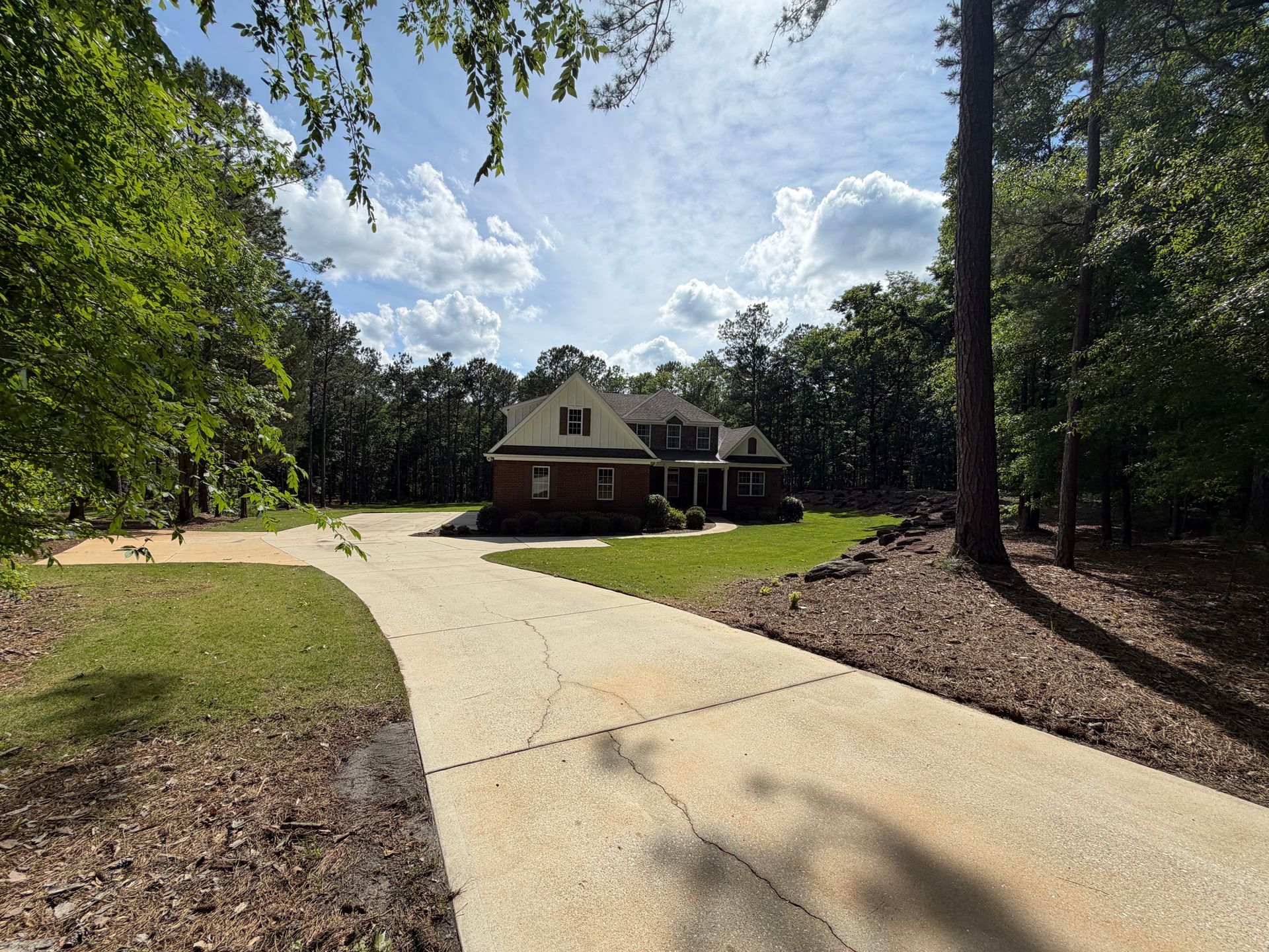 Curved driveway leading to a brick house surrounded by trees and a grassy yard