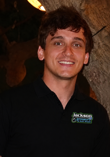 Smiling person in a black polo shirt standing outdoors near a tree at night