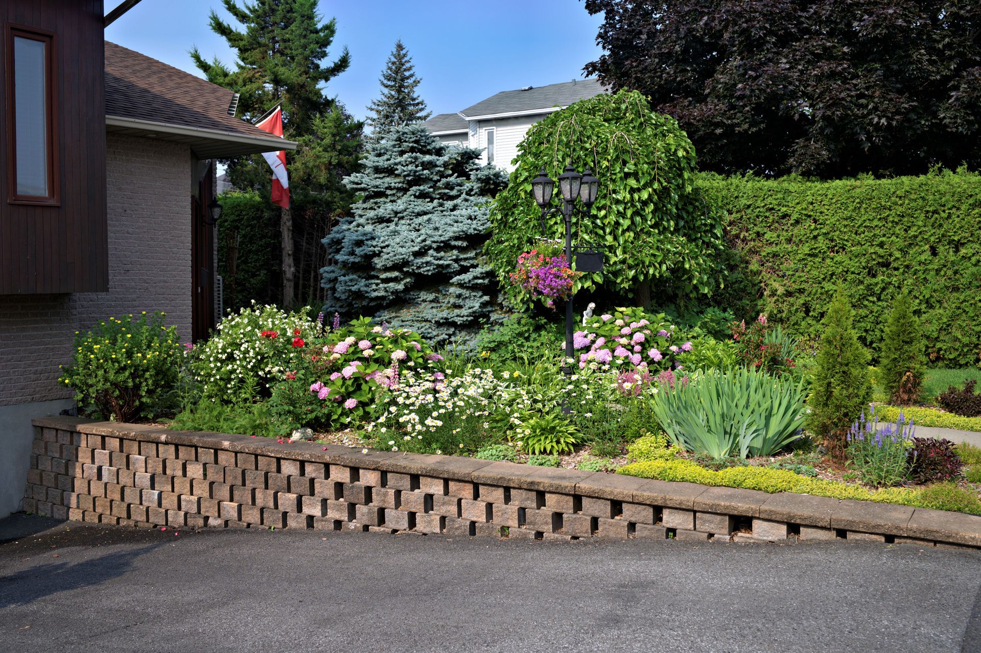 A brick wall surrounds a lush green garden in front of a house