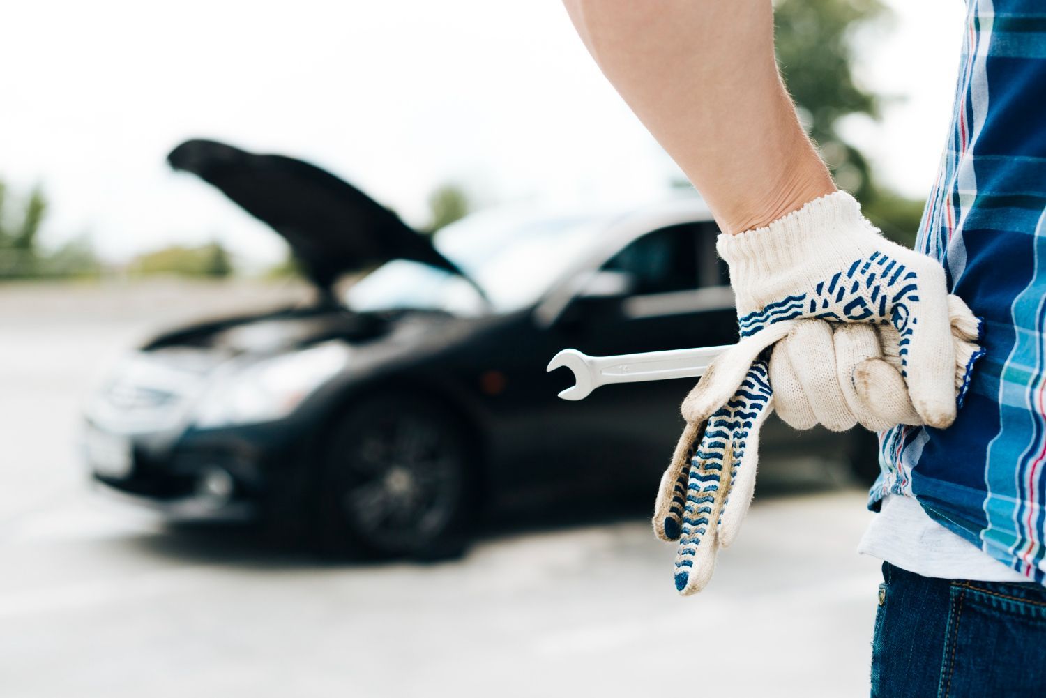 A man is holding a wrench in front of a broken down car.