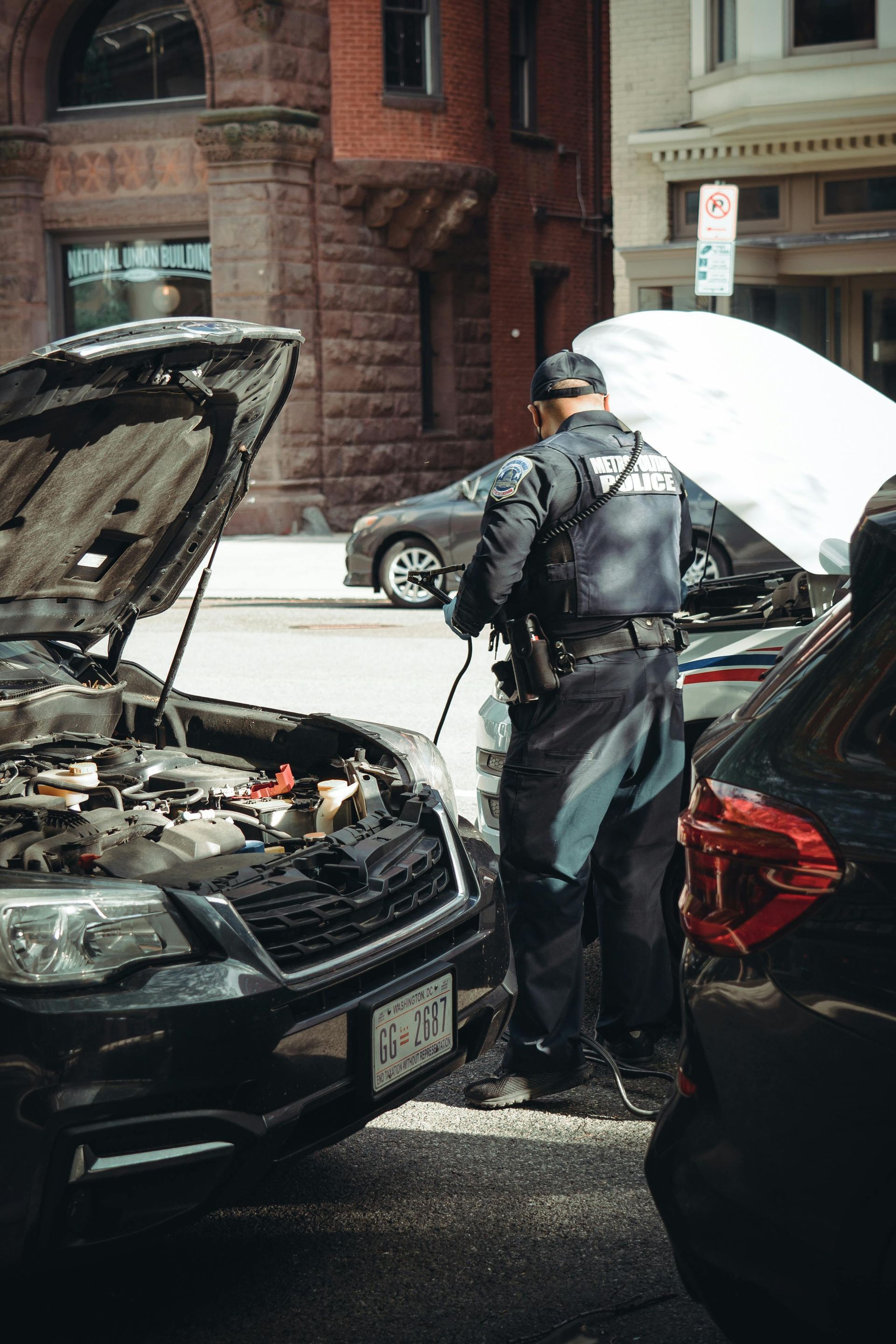 A police officer is looking under the hood of a car.