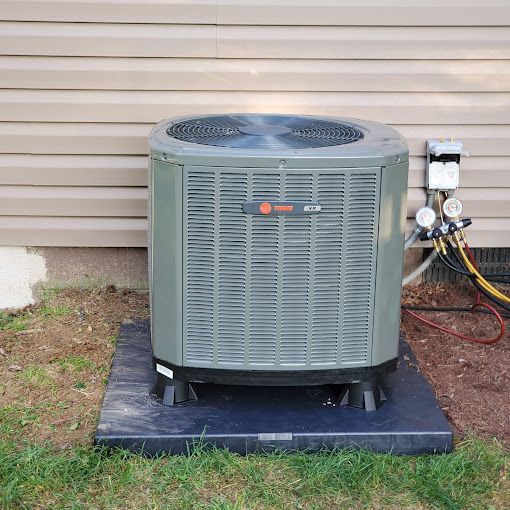 A large air conditioner is sitting on top of a black platform in front of a house.
