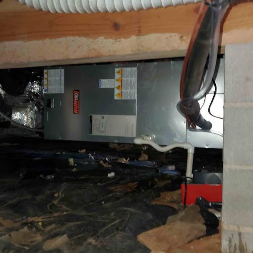 An air conditioner is sitting under a brick wall in a basement.