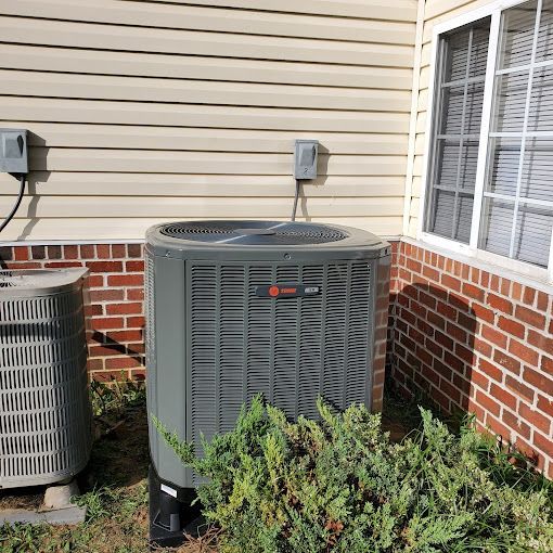 Two air conditioners are sitting on the side of a brick house.
