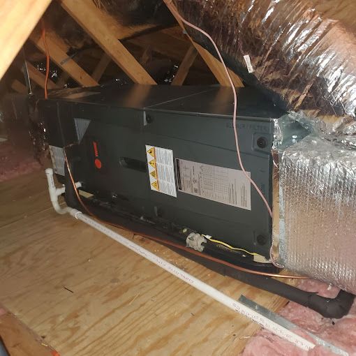An air conditioner is sitting under a ceiling in an attic.