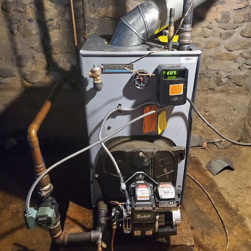 A boiler is sitting in a basement next to a brick wall.