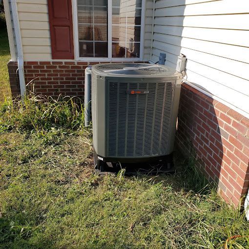 An air conditioner is sitting on the side of a brick house.